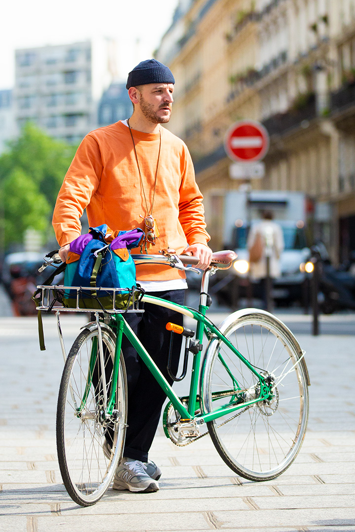 オレンジ色の服を着て自転車の側にたつ男性